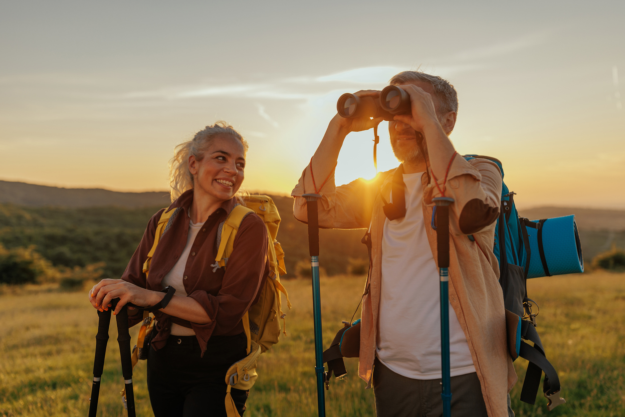 Happy middle age couple on hiking trip on summer holiday, using binoculars